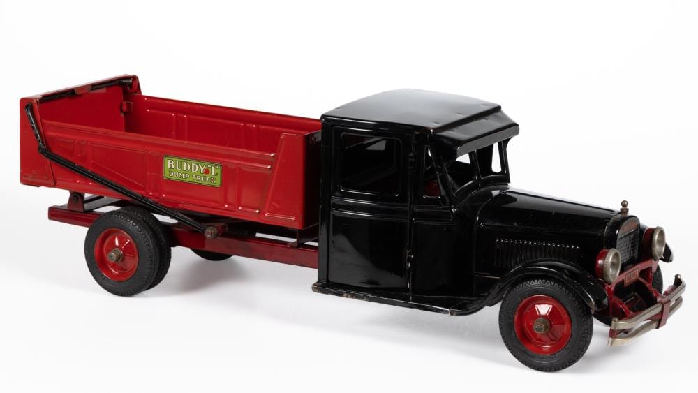 Red and black pressed-steel toy dump truck with a hinged open cargo bed and red wheel rims on a white background.