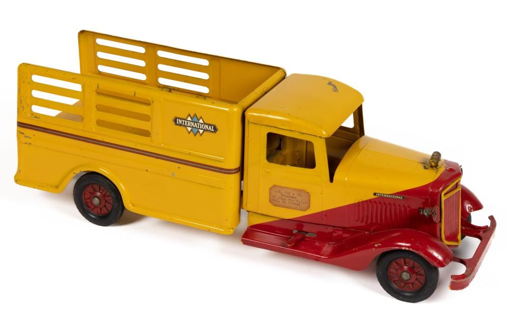 Yellow and red pressed-steel ride-on delivery service truck toy with a box cab and large wheels on a white background.