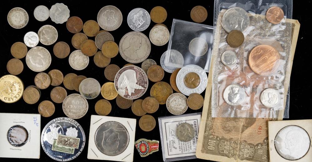Assorted coins and coin collectibles arranged on a black surface, with coin sleeves and currency notes visible.