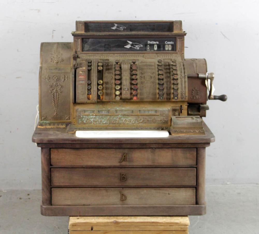 Antique brass cash register with open drawer and visible coin and currency register mechanisms behind the front panel.