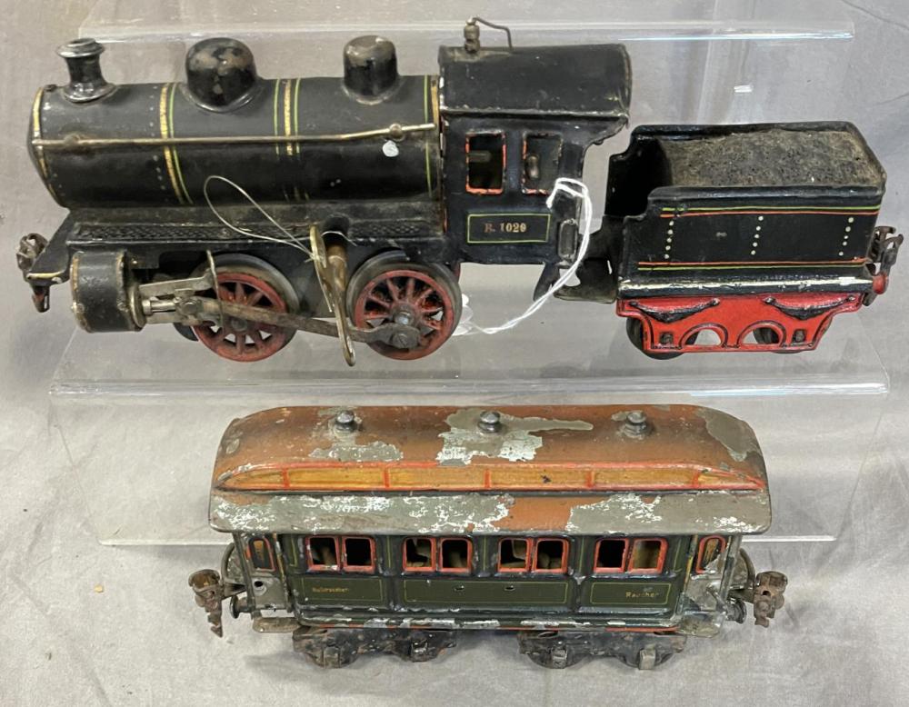 Two vintage toy rail cars on display, one steam locomotive and one passenger coach, shown side-by-side behind clear plastic covers.