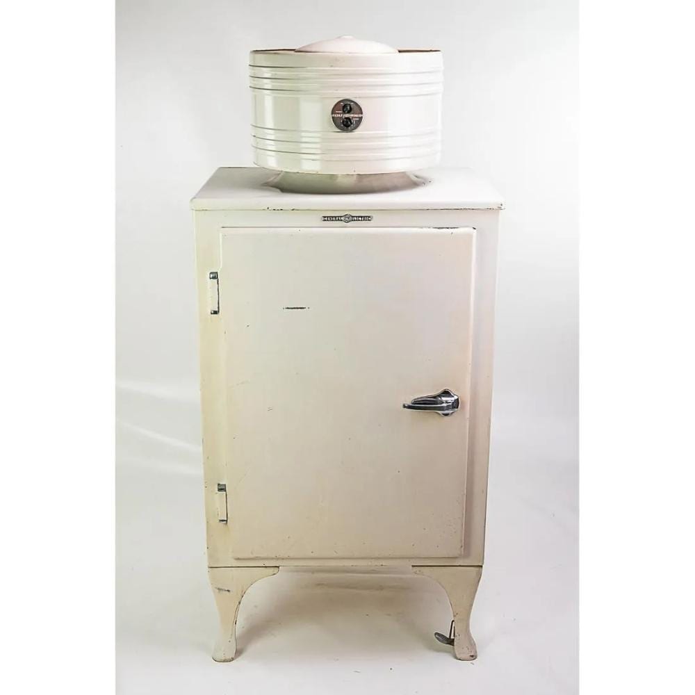 A pale refrigerator with a cylindrical mechanism mounted on top, in an auction photograph.
