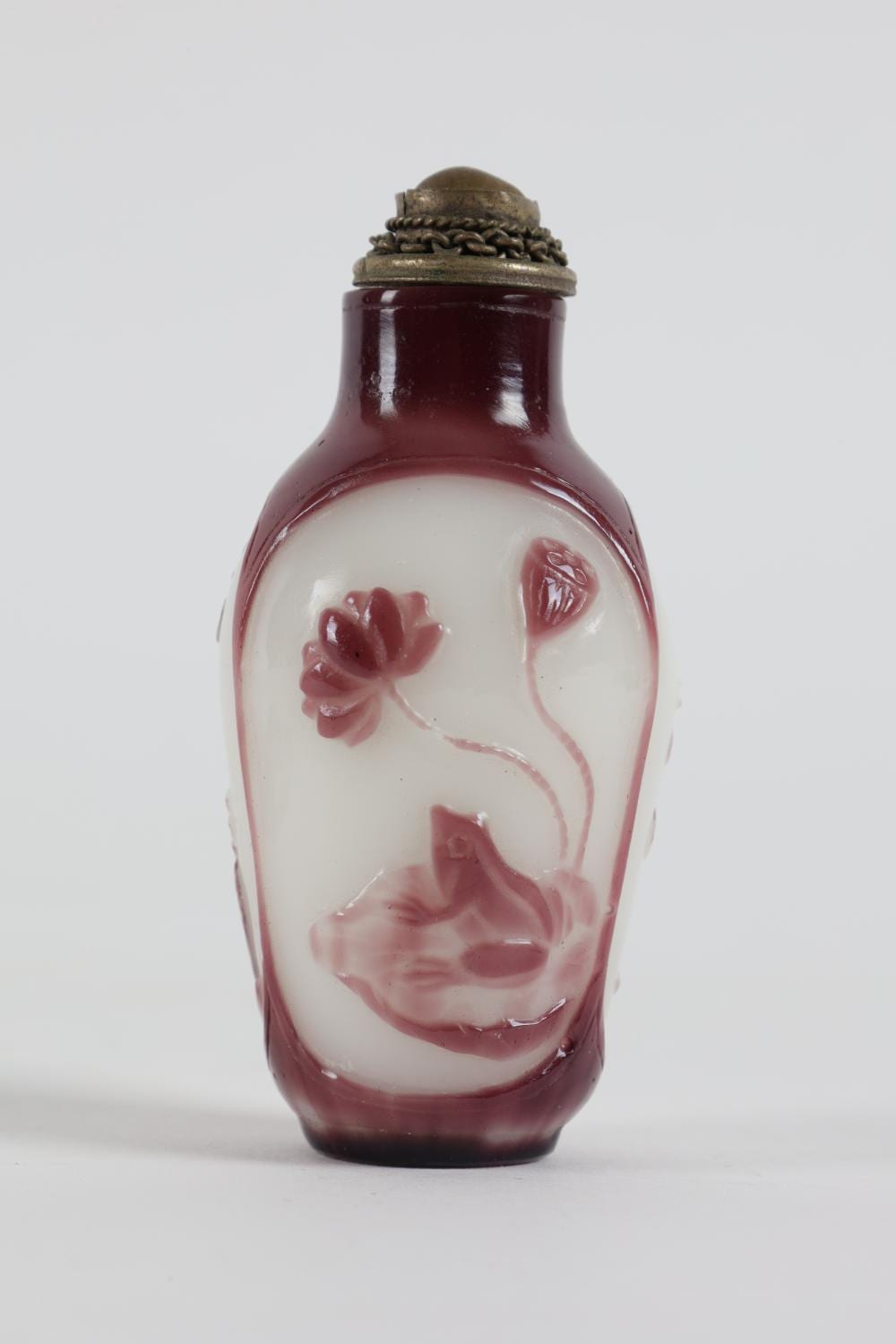 Small glass snuff bottle with maroon stopper and carved animal figures in red on the translucent body.