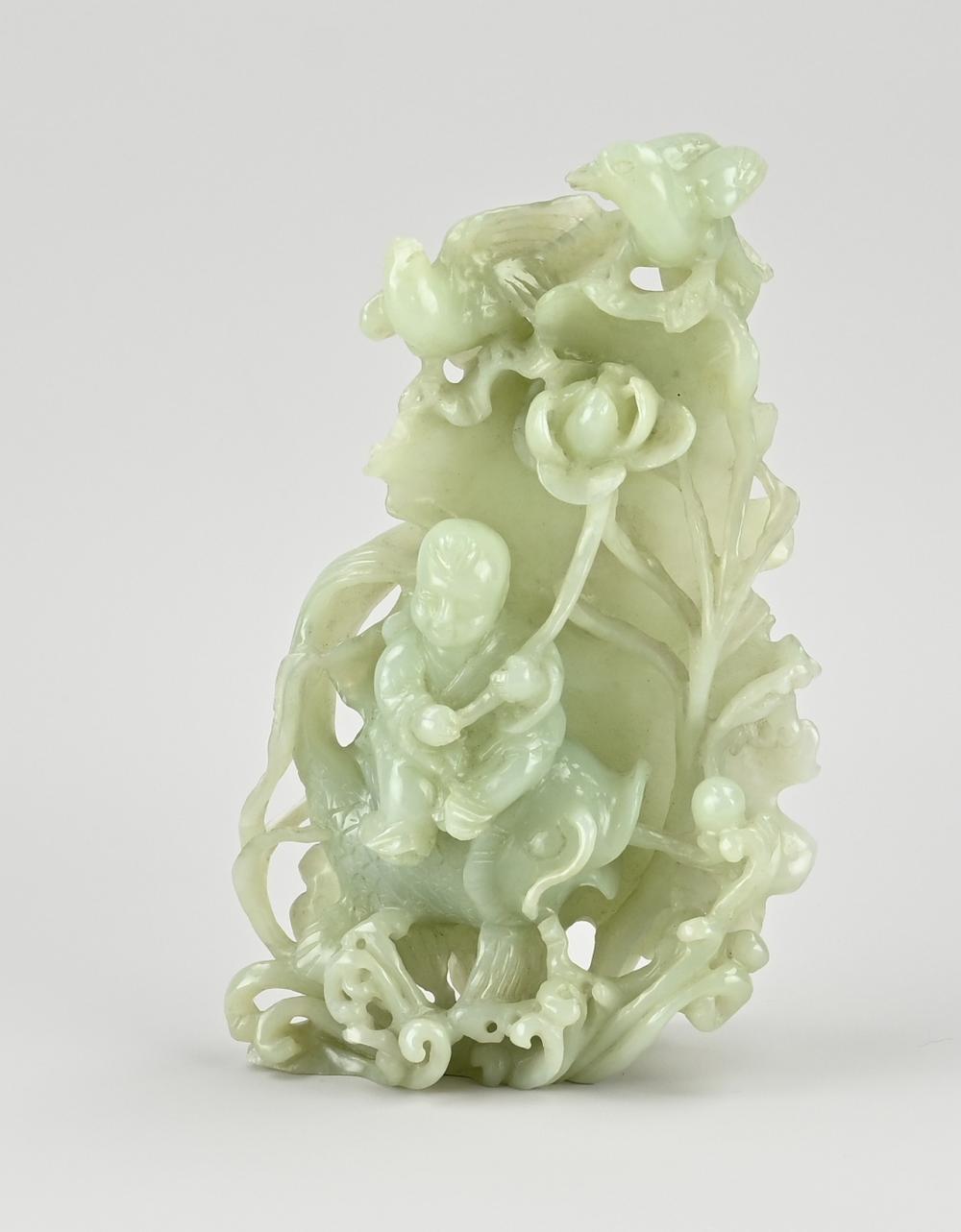 Carved light green jade sculpture with stylized figures and flowing foliage, shown against a plain background.