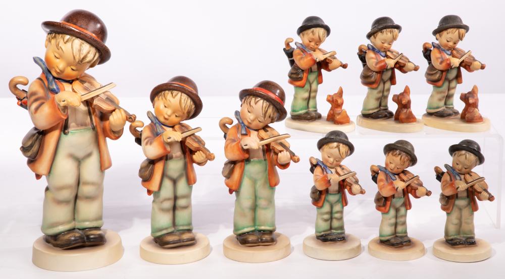 Assorted small ceramic figurines of children playing stringed instruments, wearing brown hats and colorful outfits, arranged on round bases.