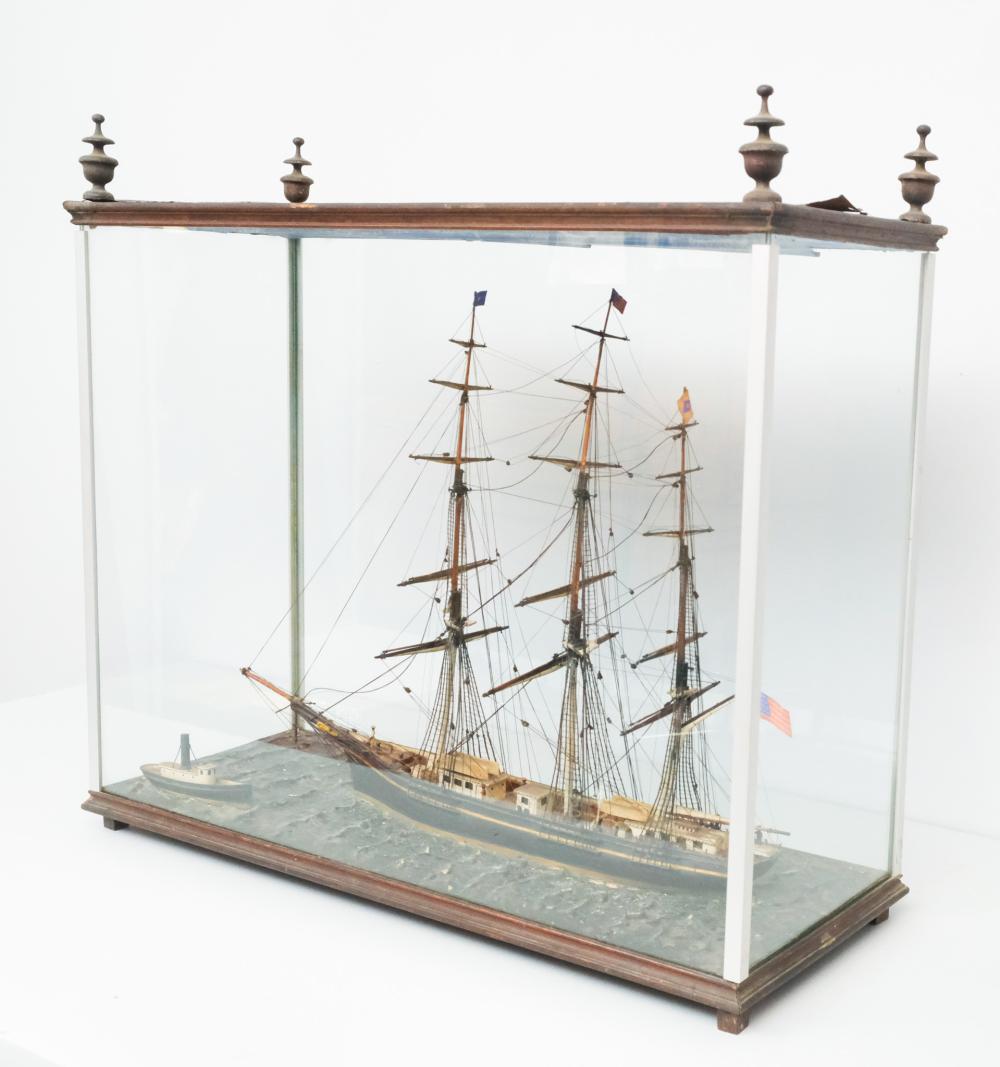Antique-style wooden model sailing ship displayed inside a glass case with detailed sails and masts.
