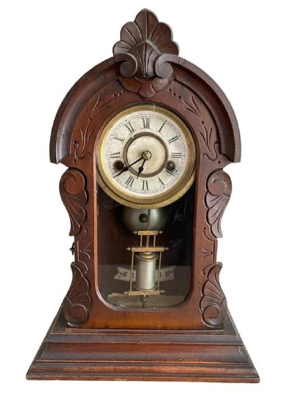 Antique style mantel clock with carved wooden case, circular dial, and Roman numerals, shown front view.