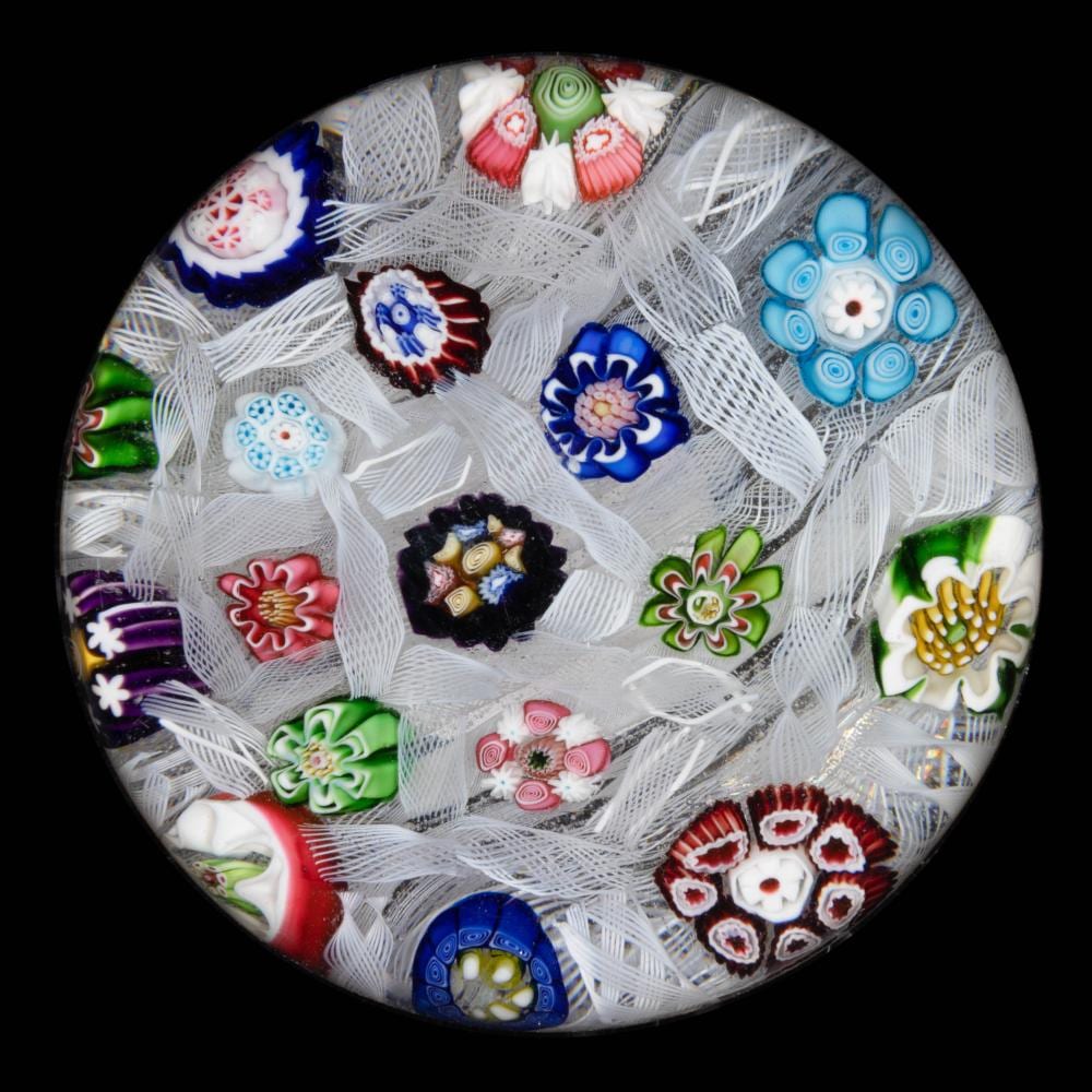 Round glass paperweight covered in small millefiori flower and geometric patterns, with a white lattice-like background.