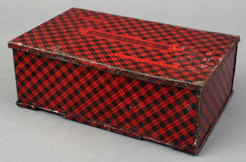 Red and black plaid folding tin lunch box with a hinged lid and metal edges, photographed on a gray background.