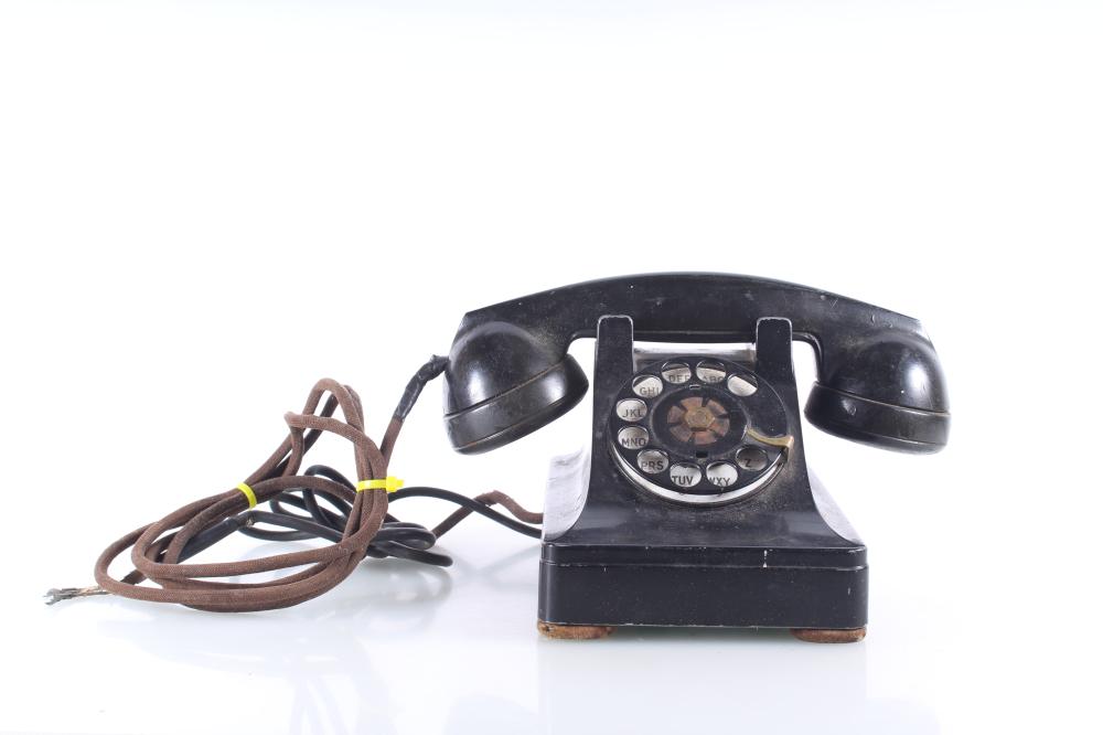 Black rotary dial corded telephone base with handset rests on a white background.