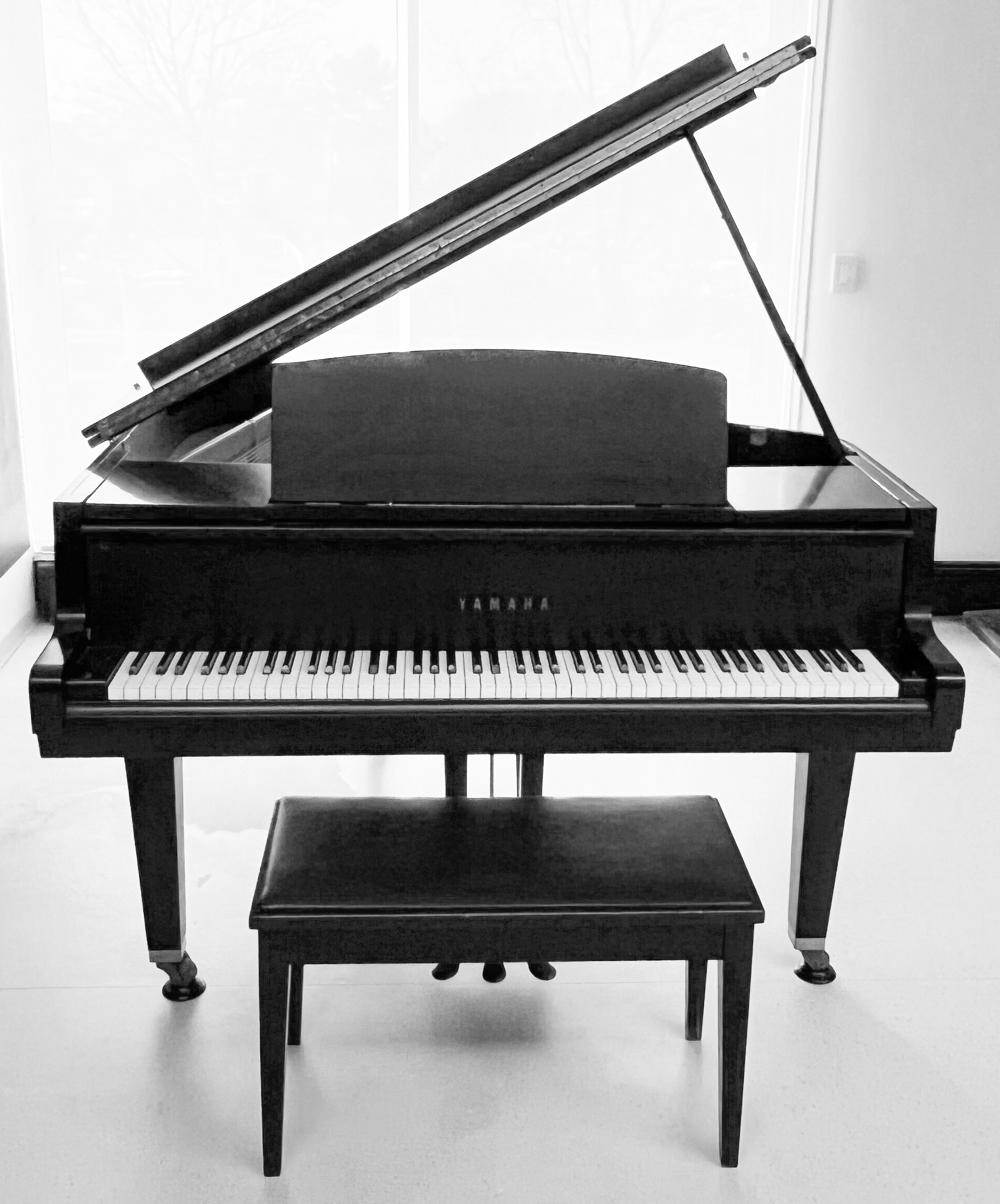 Black Yamaha upright piano with open lid and visible keyboard, shown from the front indoors.