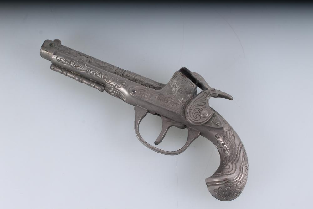 Small silver-tone toy cap gun with an ornate decorative grip and trigger, shown at a diagonal angle against a light background.