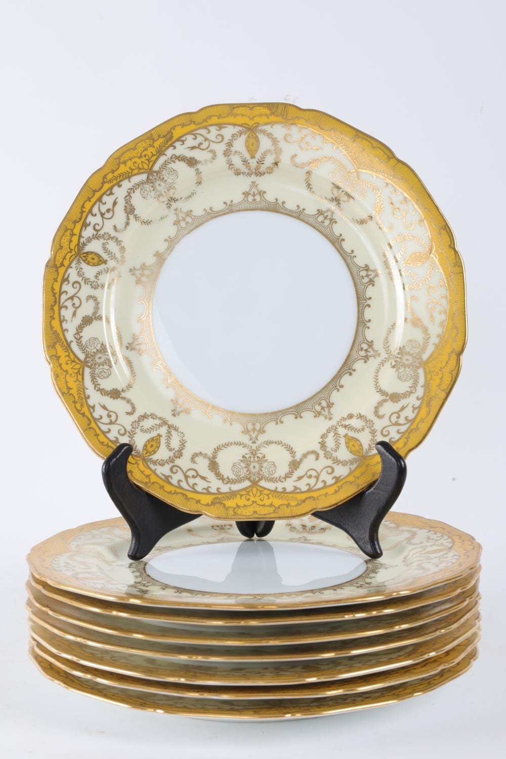 Vintage yellow and white dinner plate with gilt border and floral scroll pattern, shown on a black stand.