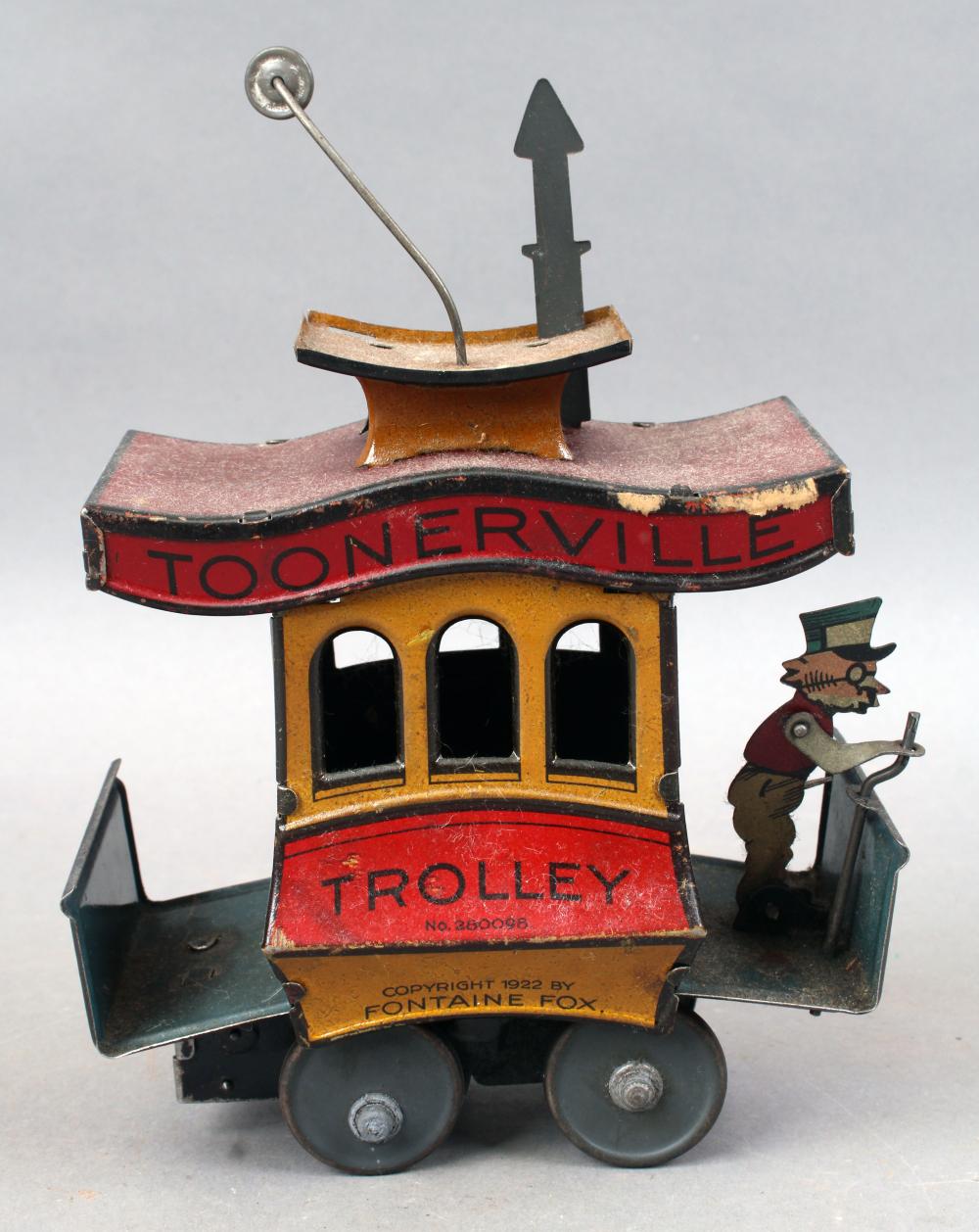 Wind-up tin trolley toy with red “TOONERVILLE” lettering, black smokestack, open windows, and a mounted fox character on the side.