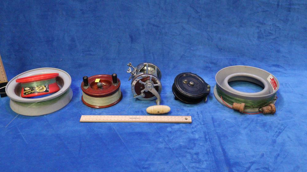 Assorted vintage fishing reel parts and spools arranged on a blue tabletop, including a large reel with crank and several line spools.