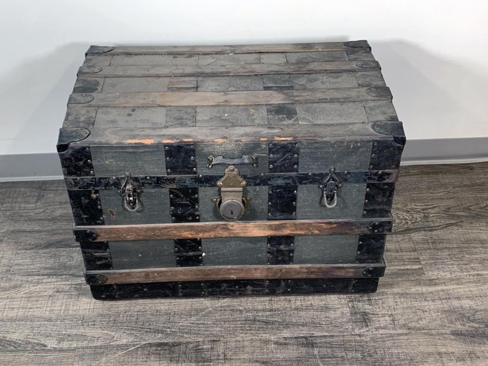 Front view of a vintage metal steamer trunk with dark panels, brass padlock, and front latch handles.