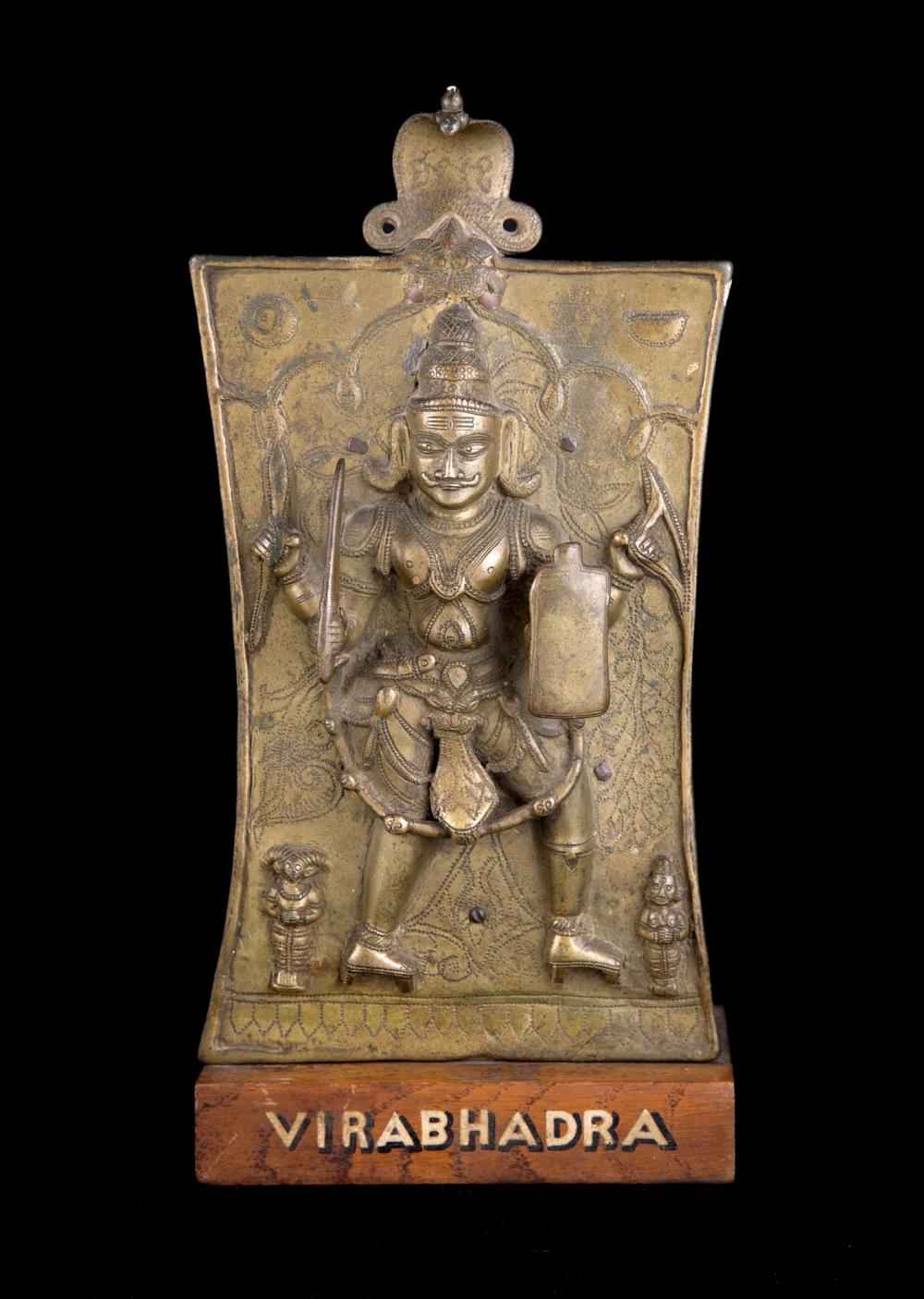 Gold-toned bronze ritual plaque featuring a seated Hindu deity with four-armed attributes, flanked by small figures, with the name “VIRABHADRA” on the base.