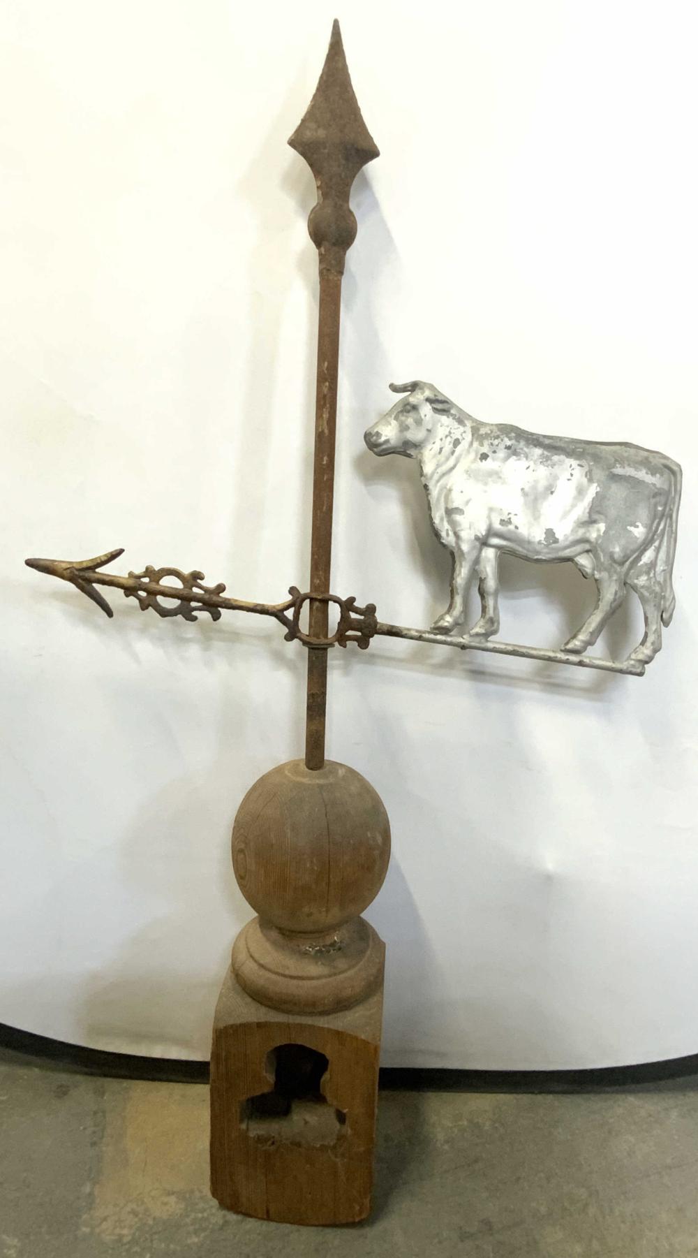 Antique cow figural weathervane mounted on a wooden post, with a metal arrow pointer and a pointed finial at the top.