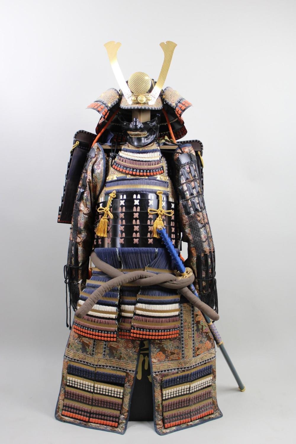 Front view of a Japanese-style samurai armor suit with helmet, layered chest plates, and a decorative sword stand.