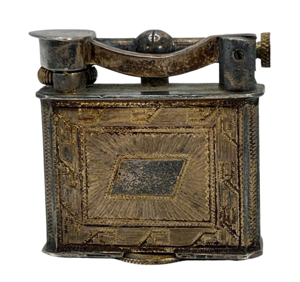 Vintage metal lift-top lighter with engraved rectangular front and side knob, photographed against a white background.