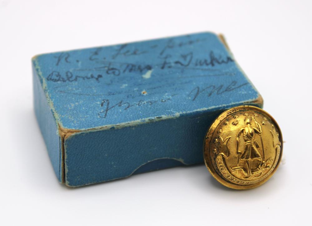 Round gold-toned metal button with an engraved rider emblem on a blue fabric-covered box.