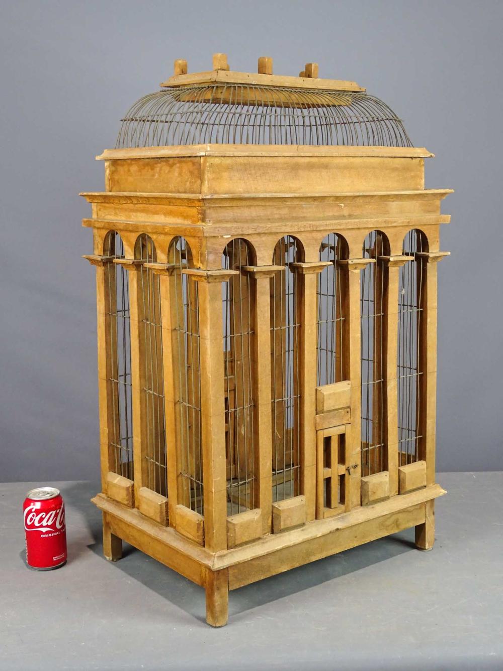 Wooden birdcage with arched top and vertical wire bars, viewed from the front against a gray background.