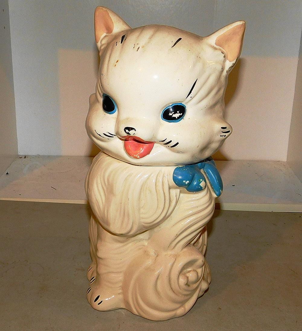 Cream-colored ceramic cat cookie jar with blue collar and paws, painted face with blue eyes and smiling mouth.
