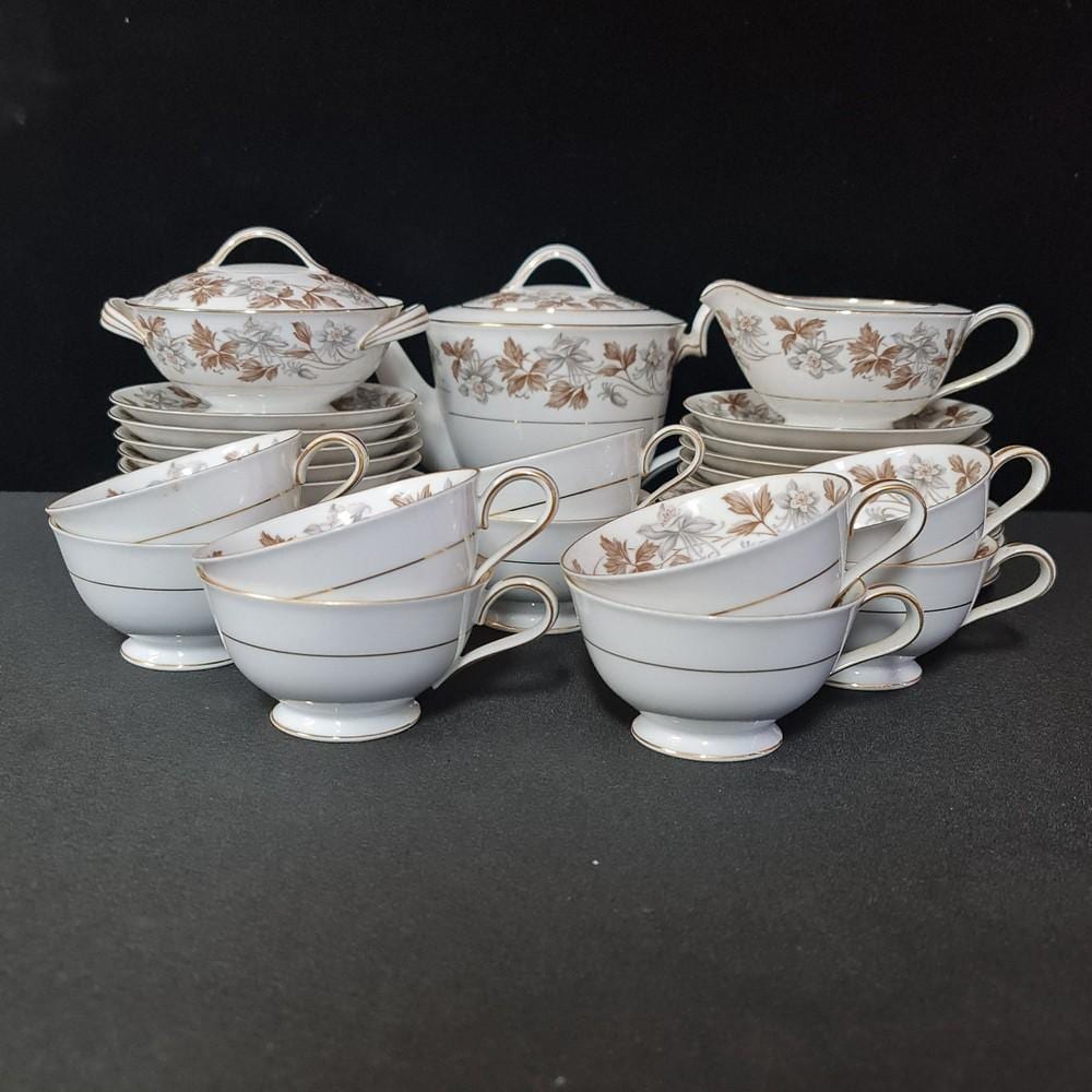 Assorted white porcelain teacups and saucers with gold trim and floral pattern, plus a sugar bowl and covered teapot on a dark background.