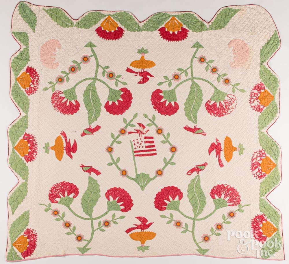 Appliqué quilt top with red, pink, and green floral and bird motifs arranged around a central patriotic shield and surrounded wreath.