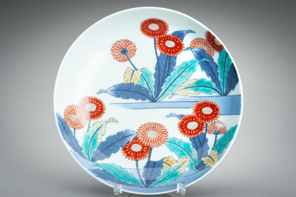 Porcelain bowl with a white background and painted red-orange and white flowers with blue-green leaves around the rim and interior.