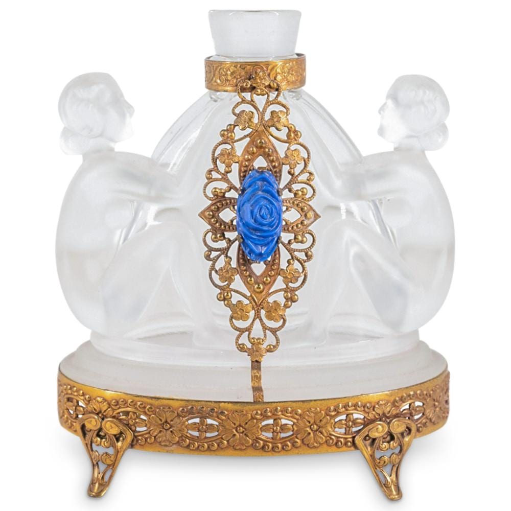Clear glass perfume bottle with ornate gold mounts, blue decorative rose centerpiece, and two white cherub figures on the sides.