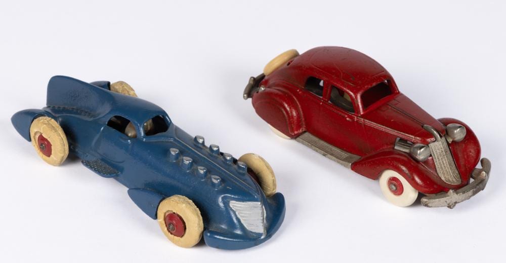 Two vintage toy cars shaped like classic models: one blue open-cockpit car and one red car with chrome front details, on a white background.