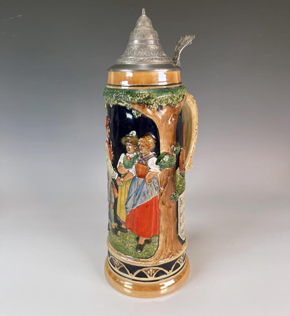 Tall German beer stein with a hinged lid and pewter top, decorated with painted figures and a tree on a brown background.