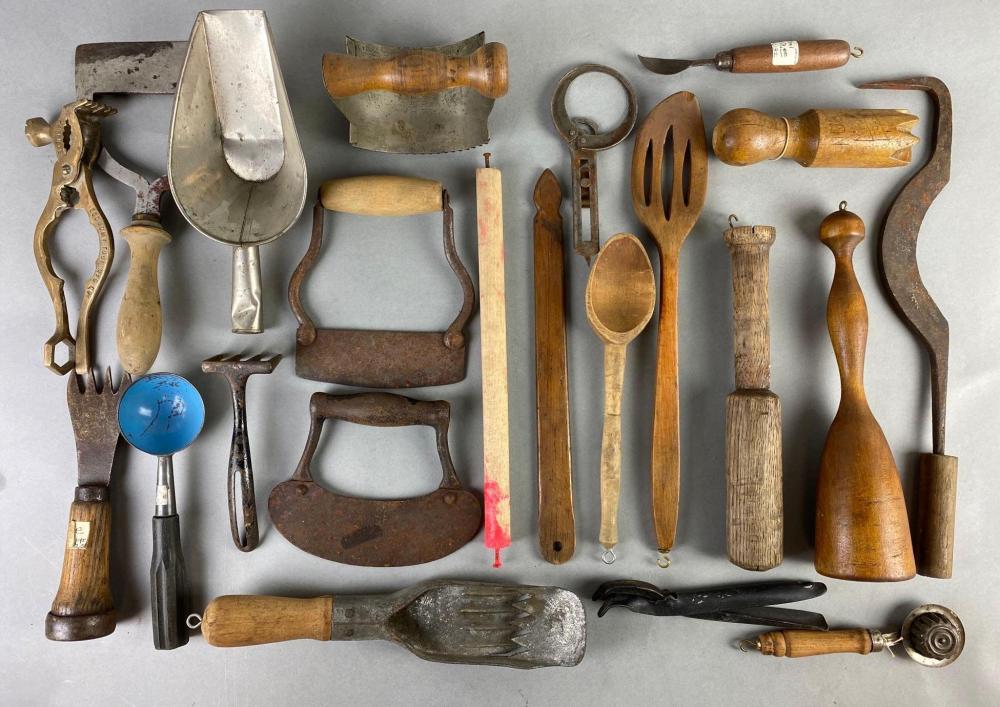 Assorted vintage kitchen utensils arranged on a gray background, including wooden-handled tools, metal scoops, and a ball-shaped handle.