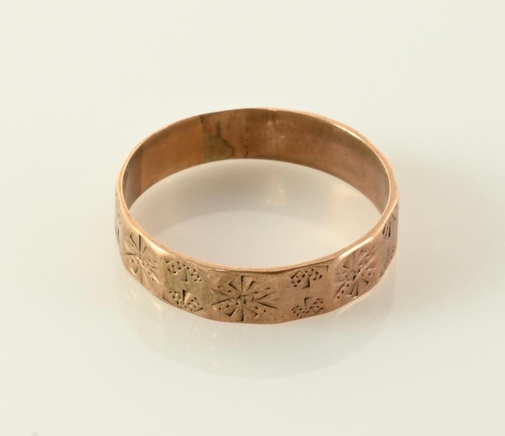 Close-up of a gold wedding band ring with engraved floral and geometric patterns on the band.