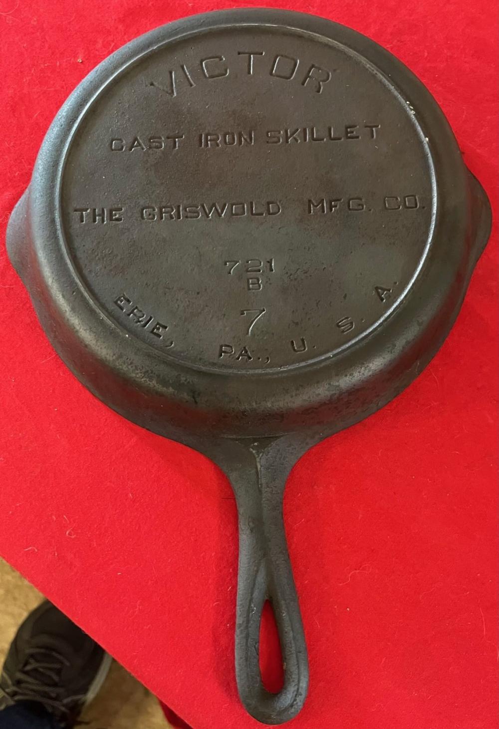 Cast iron skillet with embossed “VICTOR” and “The Griswold Mfg. Co.” lettering, shown from the underside on a red background.