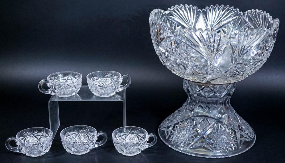 Cut glass punch bowl with matching small cups in a diamond-and-fan pattern, shown on a dark background.