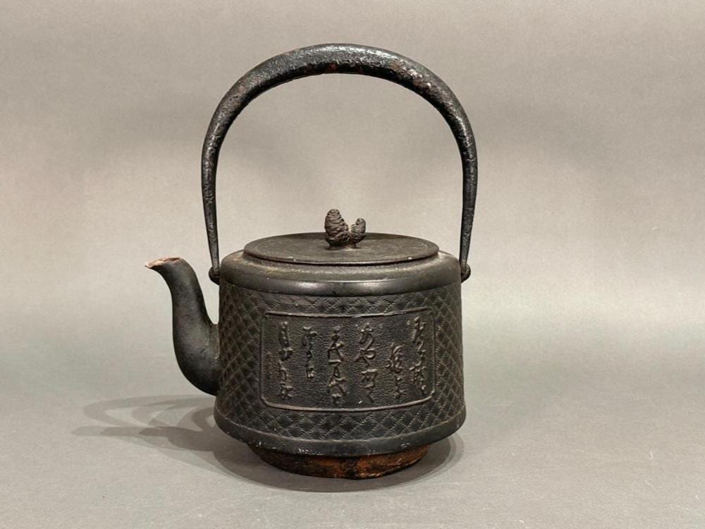 Cast iron kettle with arched handle and round lid knob, decorated with raised panels and characters on the body.