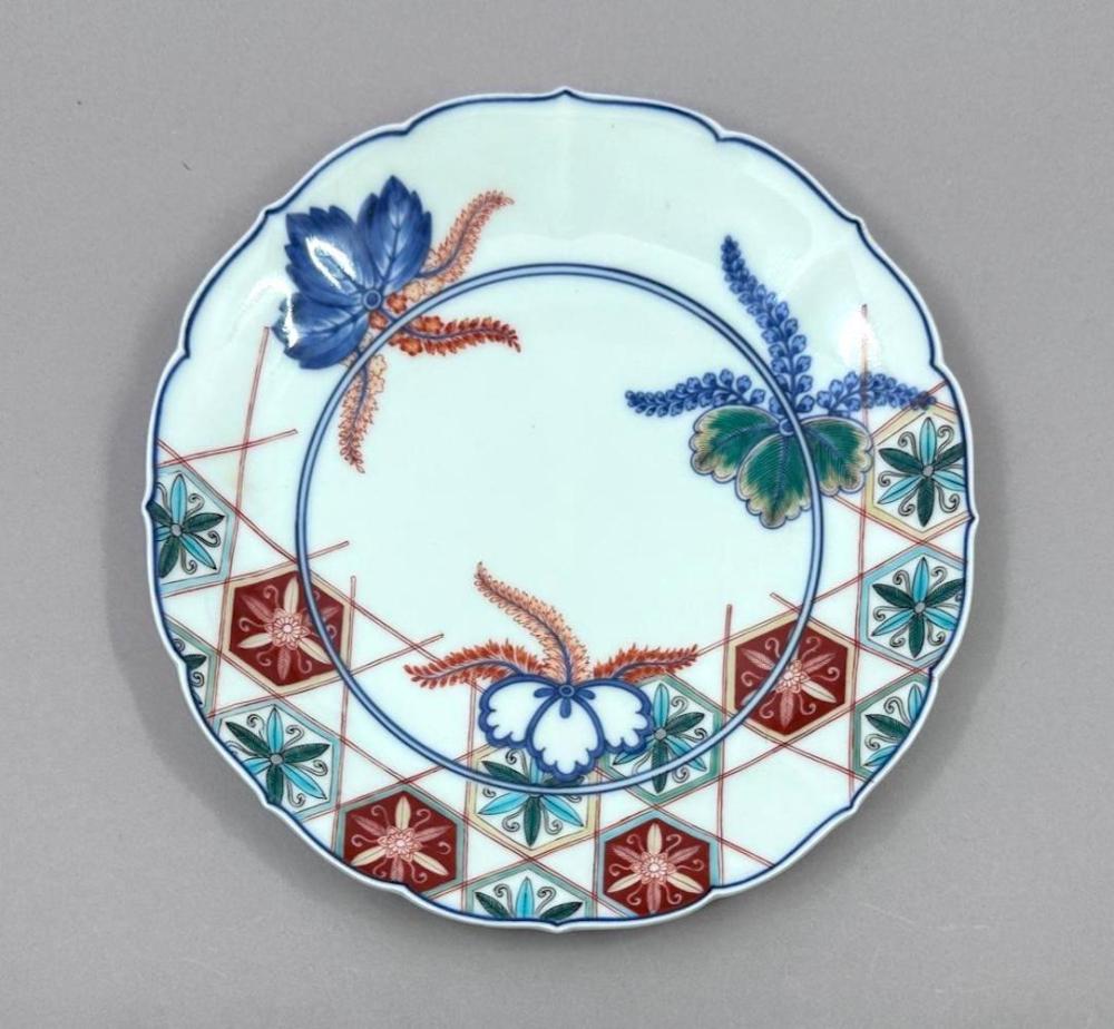 Japanese porcelain decorative plate with blue floral and leafy designs, red and green diamond-pattern border, and scalloped rim.