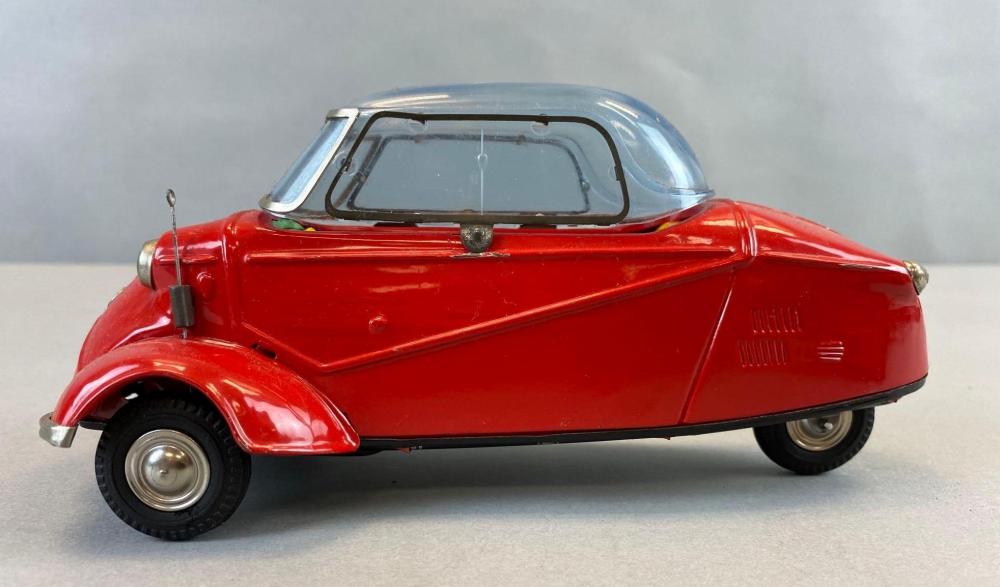 Red vintage friction toy car with a clear windshield, black wheels, and a blue-gray roof section shown in left side view.