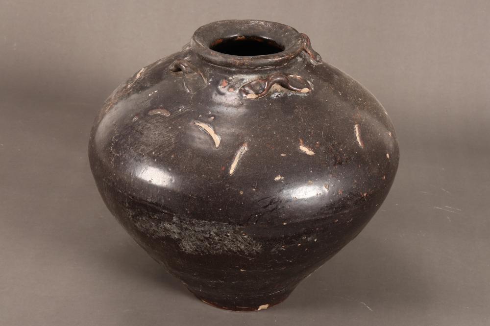 Small dark ceramic jar with an open mouth and a few applied decorative motifs near the shoulder, photographed against a neutral background.