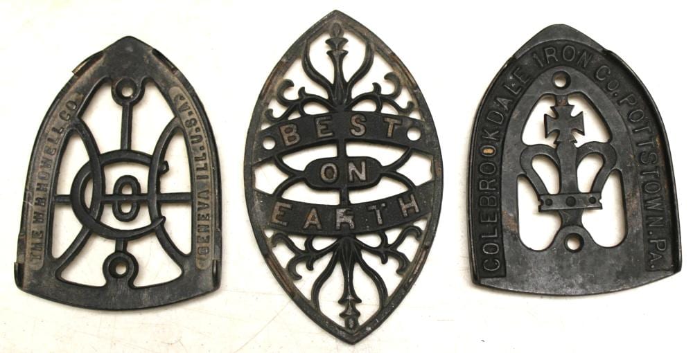 Three black cast-iron trivet bases with horseshoe-shaped frames and decorative cutout designs.