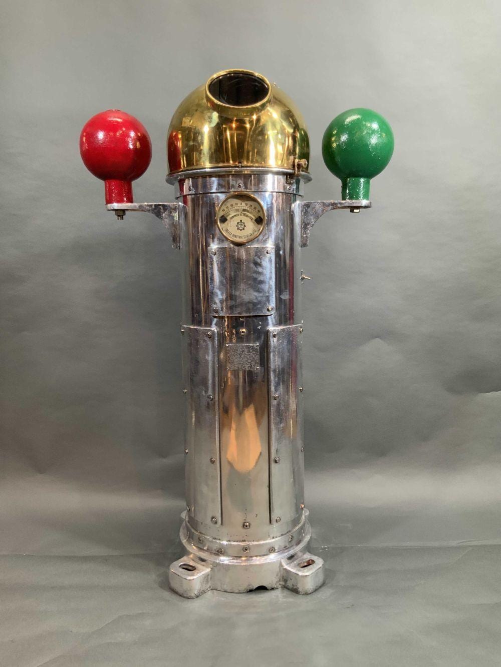 Brass and silver metal binnacle with a circular compass dial and two colored control knobs, red left and green right.