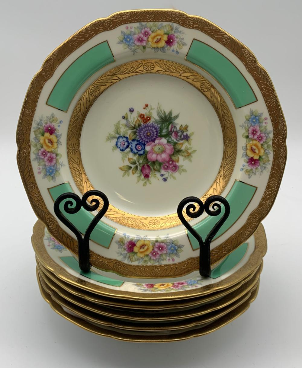 Set of floral porcelain soup plates with gold border, teal geometric panels, and colorful flower bouquets on white centers, shown stacked with black display eas