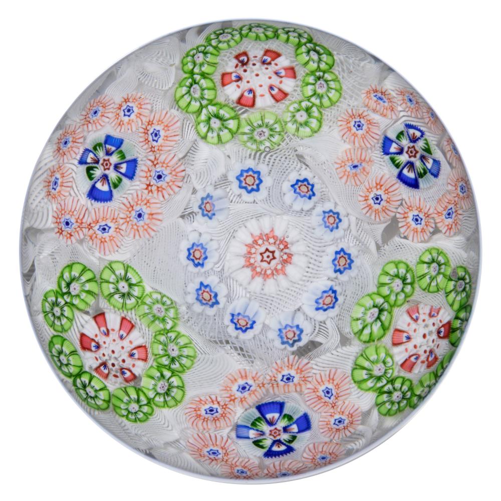 Round clear glass paperweight with millefiori pattern of small colored flowers and star shapes in green, blue, red, and white.