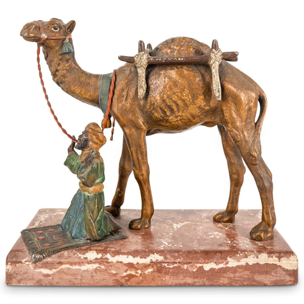 Bronze-colored camel-like animal sculpture with painted clothing and a small kneeling figure on a rectangular base.