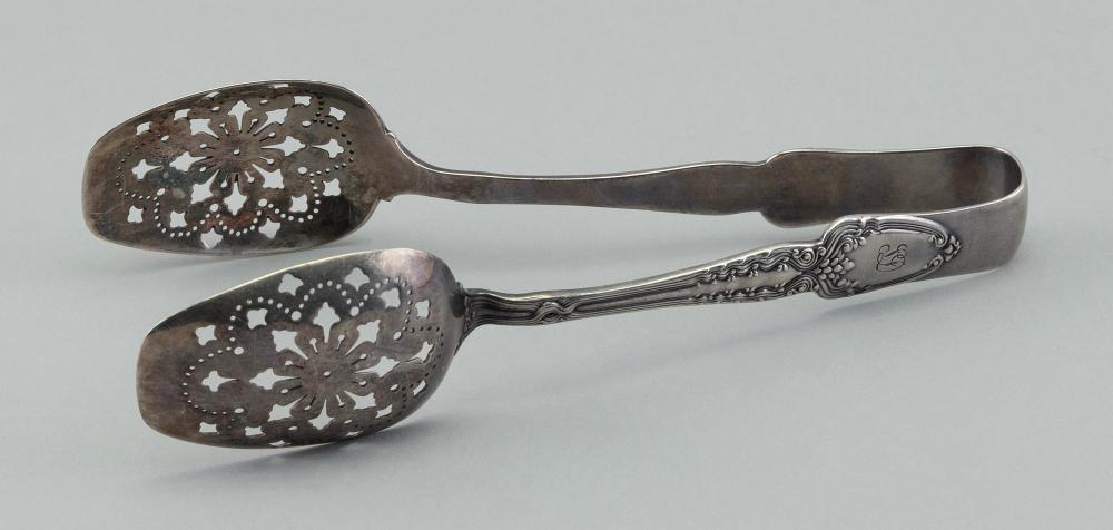 Close-up of a pair of silver-tone serving ice tongs with pierced floral metalwork on the spoon-shaped ends and an engraved handle.