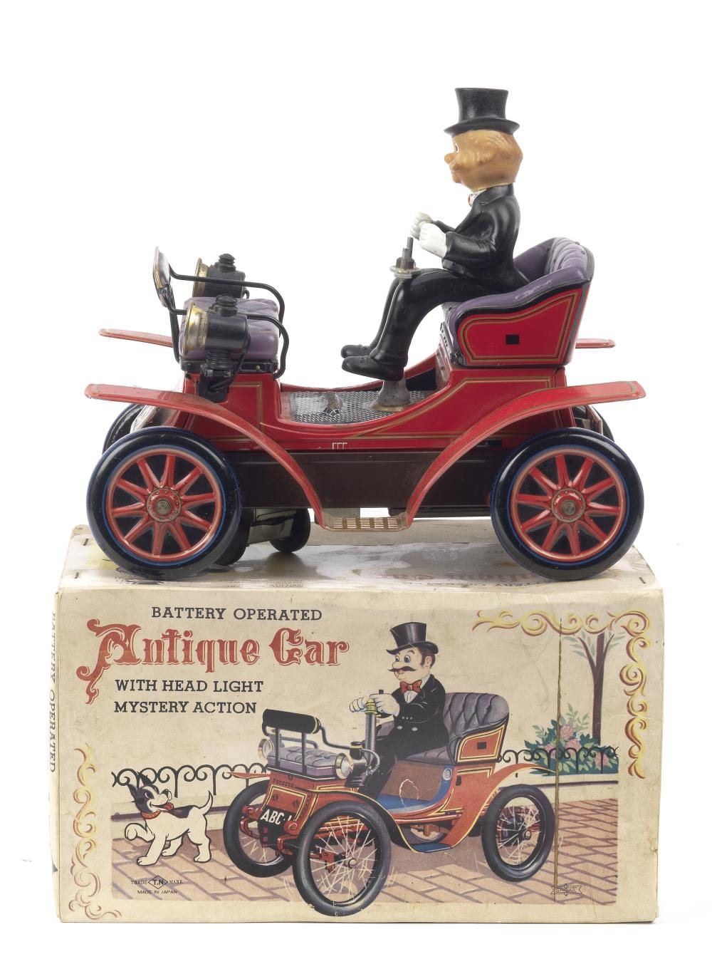 Tin-plate antique car toy with a seated man figure, head light, and purple-red body, shown on top of its original cardboard box.