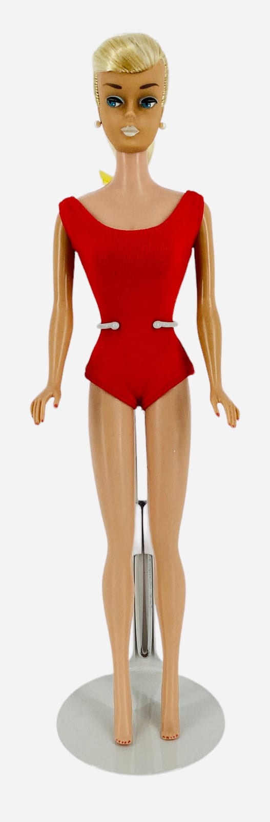 Fashion doll shown full body with blonde updo hair and blue eyes, wearing a red one-piece swimsuit and white suspenders, posed on a stand.