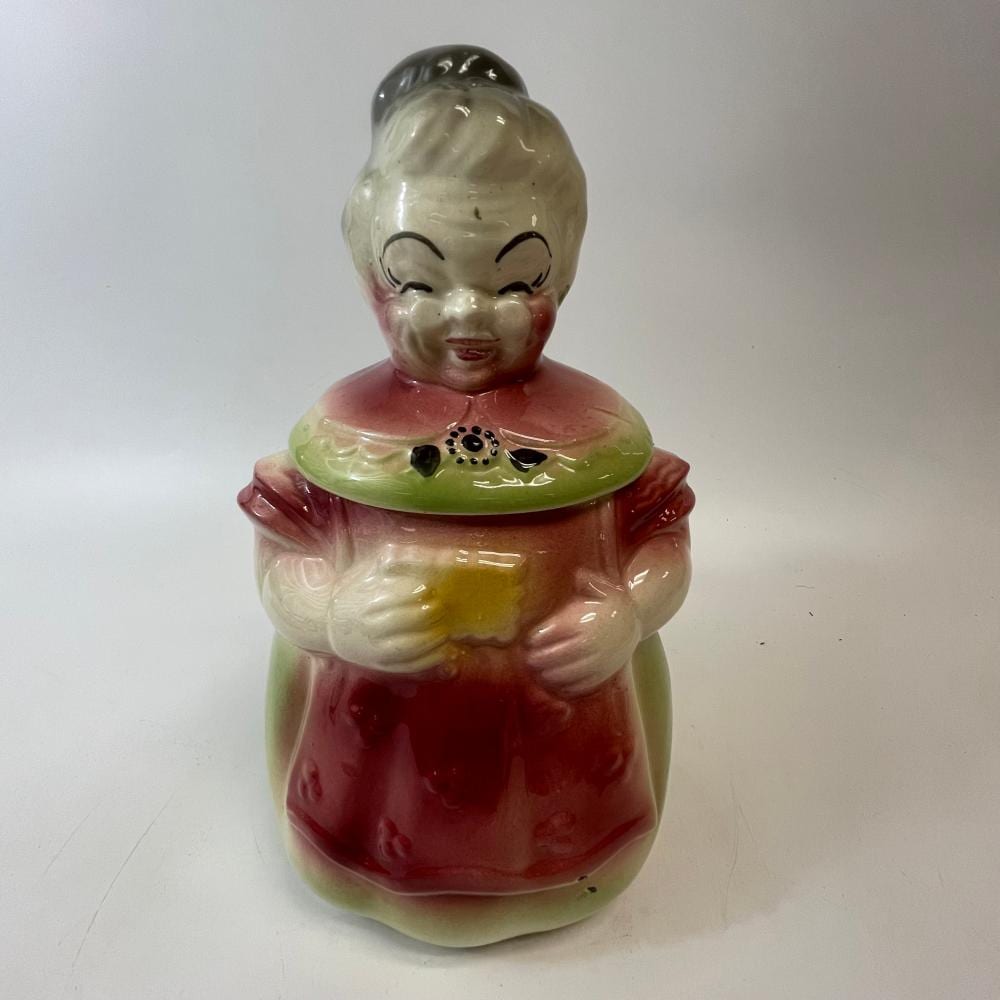 Vintage ceramic cookie jar shaped like a woman with a painted face, dark hair, and a red and cream dress, with a hinged lid.